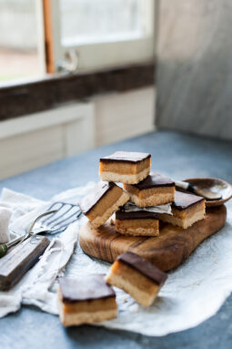 sliced caramel slice piled up on a wood trivet next to window