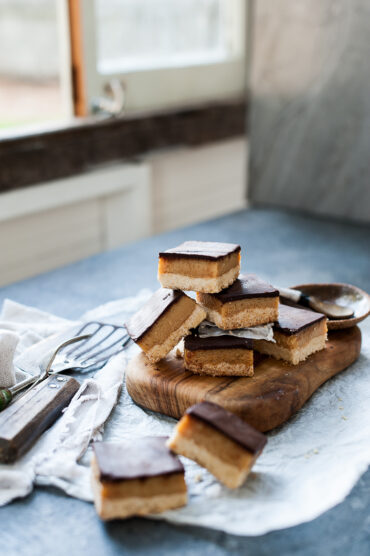 sliced caramel slice piled up on a wood trivet next to window